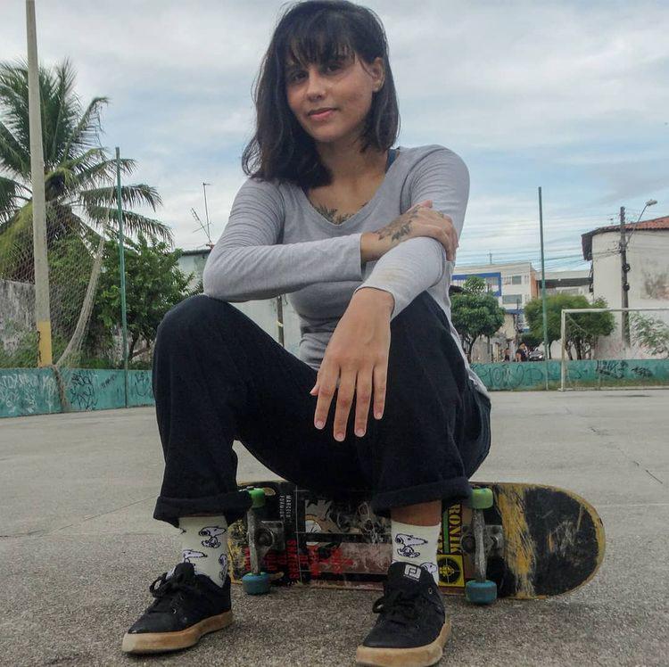 uma mulher posa para foto sentada em um skate